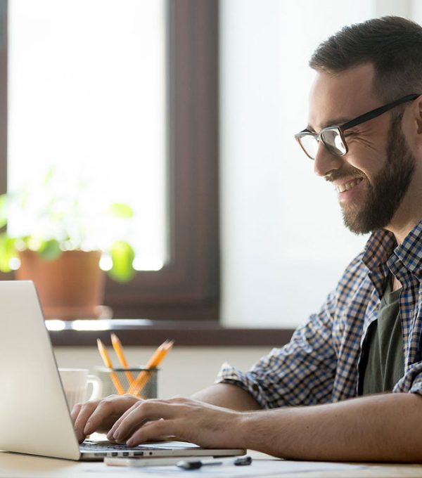 Persona sentada en un escritorio trabajando en una computadora con una tasa y un lapicero.