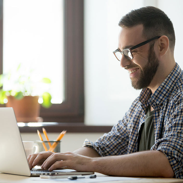 Persona sentada en un escritorio trabajando en una computadora con una tasa y un lapicero.