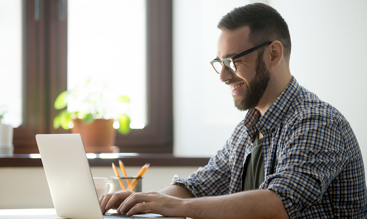 Persona sentada en un escritorio trabajando en una computadora con una tasa y un lapicero.