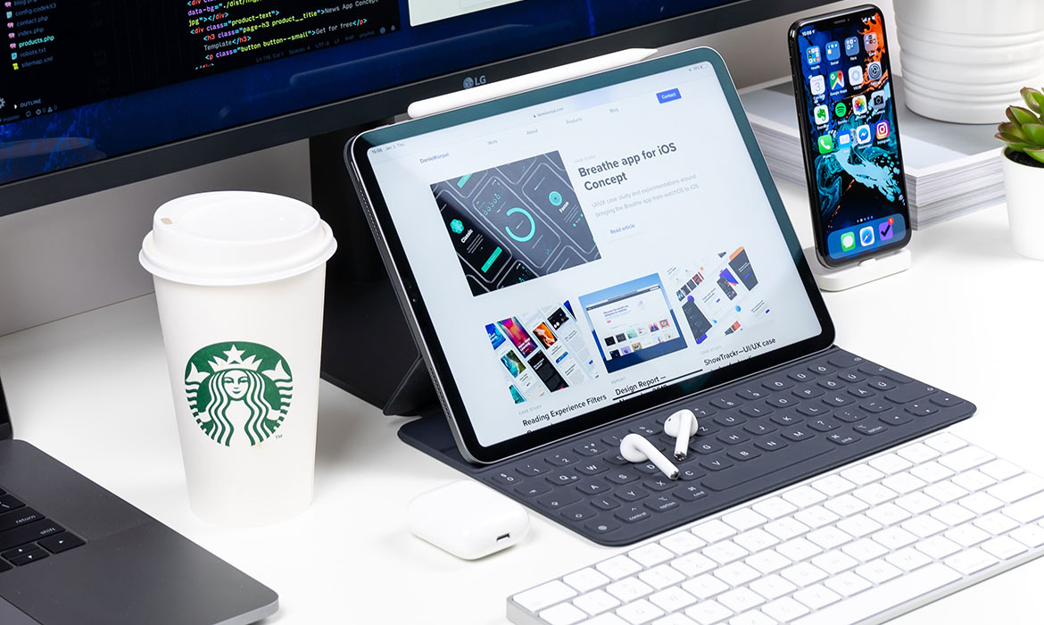 Setup con vaso de café, un iPad con funda y teclado y un iPhone sobre una mesa con unos airPods.